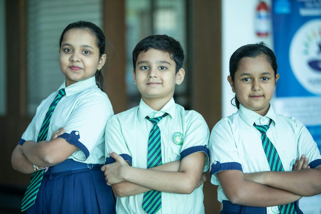 Three Indian school students posing confidently in uniform indoors.
